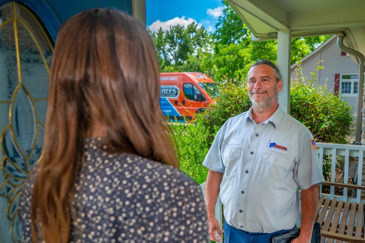 A 72 Degrees technician in uniform greeting a homeowner at her front door, with the service van parked at the kerb