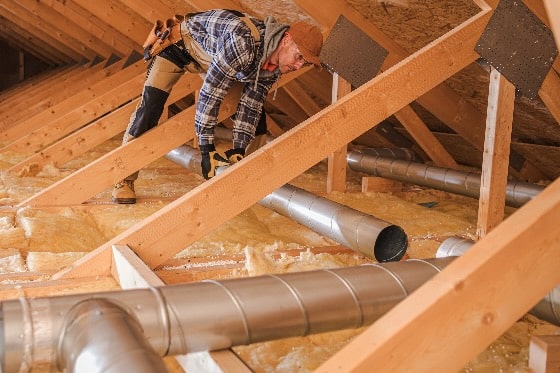 A person installing ducts in an attic