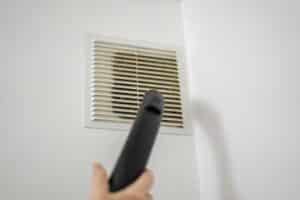 A person using a vacuum cleaner extension to clean the air vents on the wall