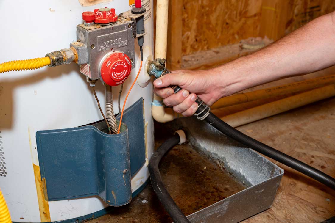 A plumber's hand attaching a hose to a water heater before draining it