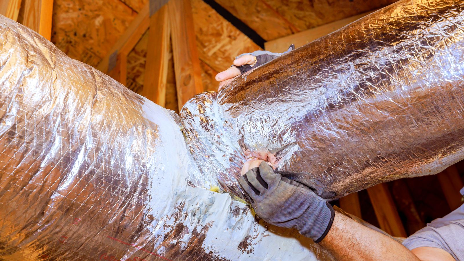 An HVAC technician reattaching a duct to seal leaks
