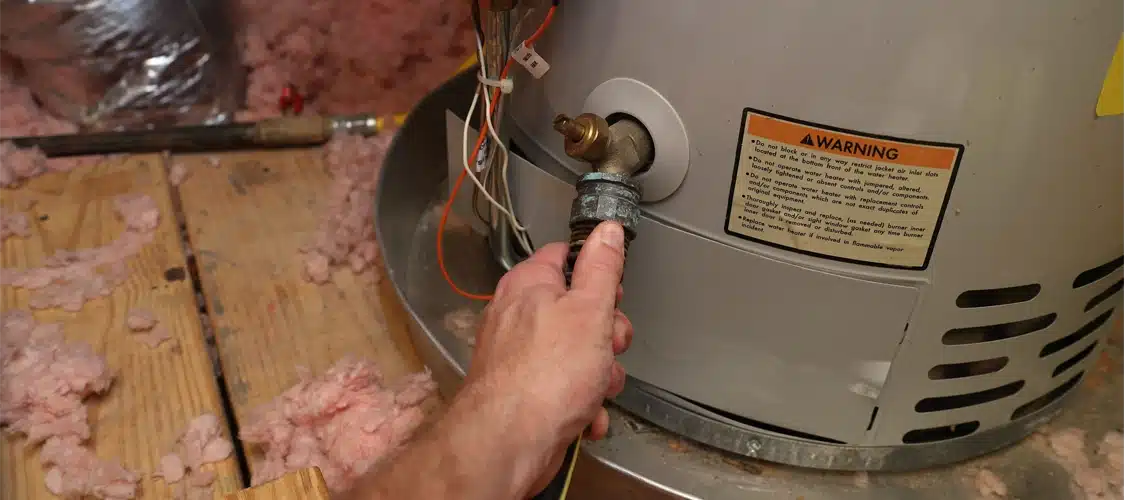 A plumber attaching a hose to flush a water heater located in a home's attic
